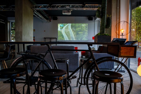 A modern bar area with a projection screen displaying a road map, a bicycle, and stools. - Sport Hotel Gym + SPA (Covilhã)