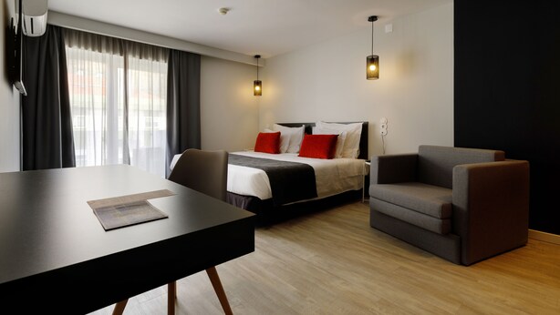 A modern hotel room with a bed, a sofa, a dining table, and a TV. - Sport Hotel Gym + SPA (Covilhã)