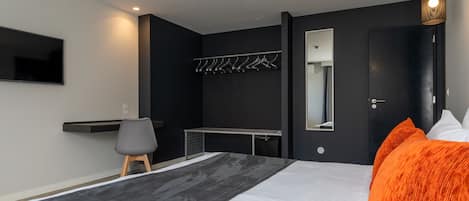 Ein modernes Schlafzimmer mit einem Bett, einem Schreibtisch, einem Stuhl, einem Fernseher, einem Kleiderhaken und einer Tür.