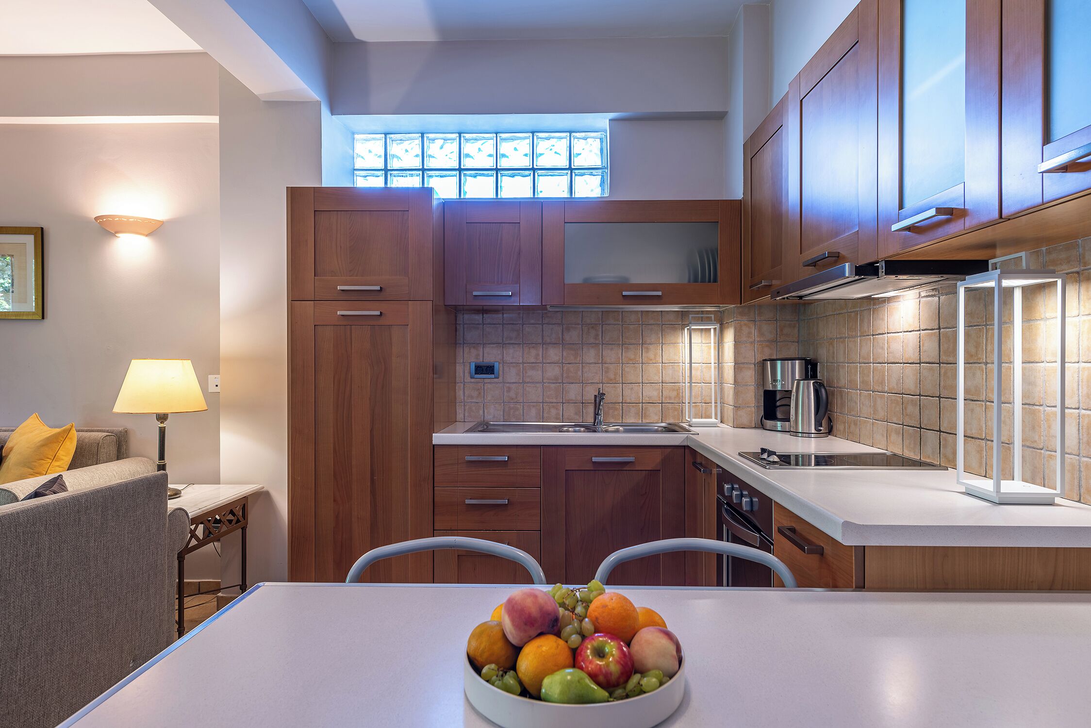 Una cocina moderna con armarios de madera, una encimera blanca y un frutero sobre la mesa.