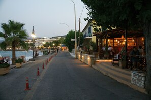 Une rue côtière bordée de terrasses, de palmiers et d’un bar offrant une vue sur la mer.