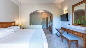 A hotel room with a large bed, a wooden desk, a bench, a TV, and a mirror.