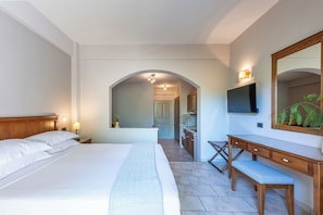 Een hotelkamer met een groot bed, een houten bureau, een bankje, een televisie en een spiegel.
