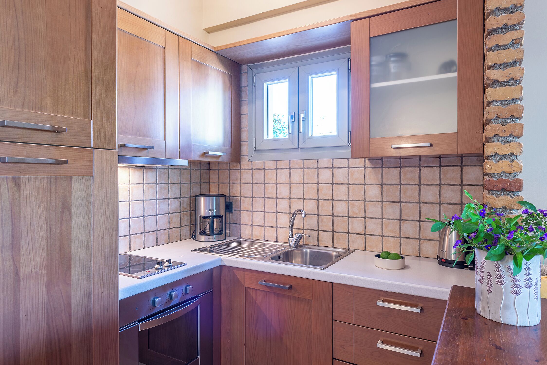 A kitchen with wooden cabinets, a stainless steel sink, a coffee maker, and a potted plant.