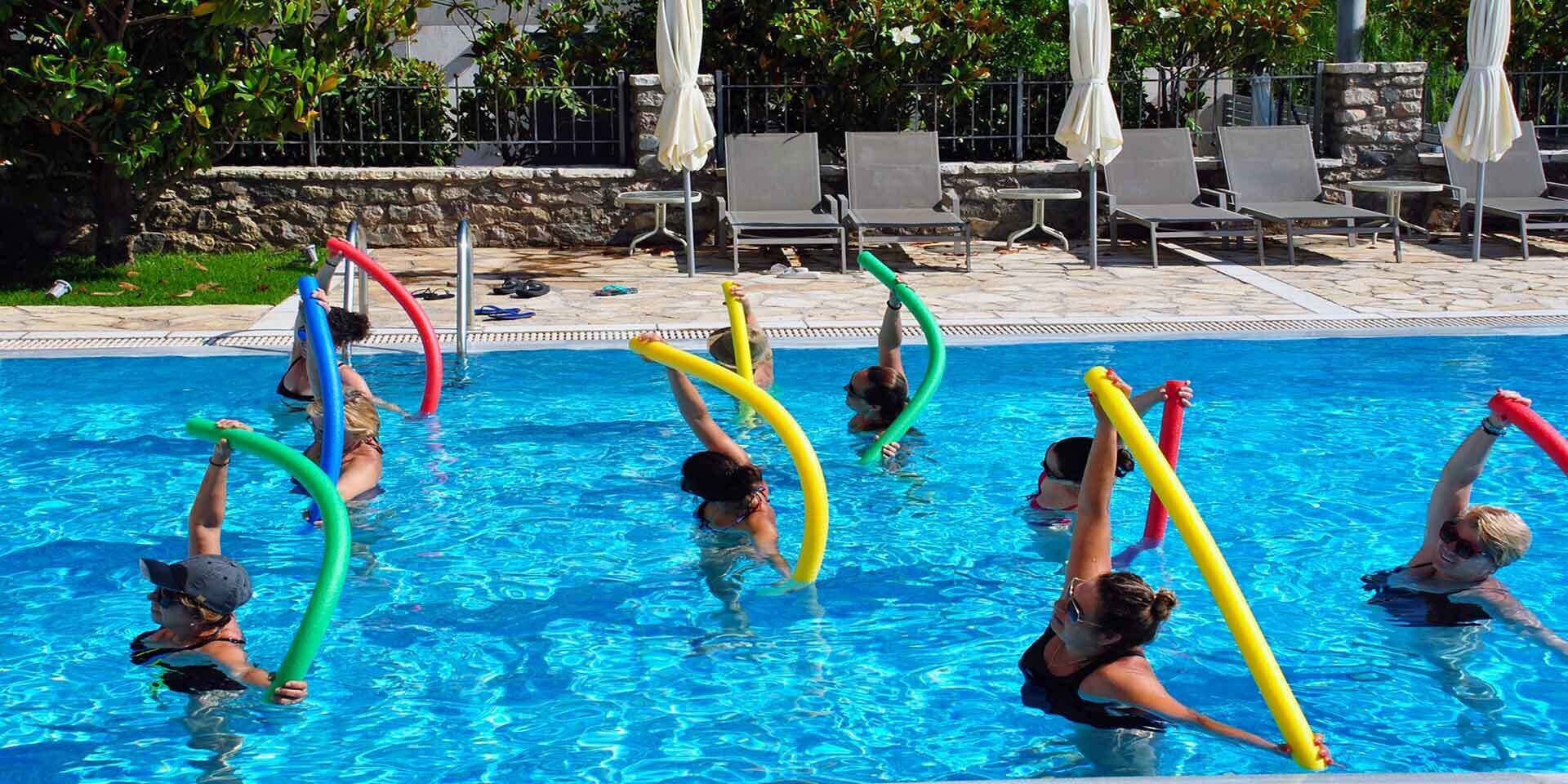 A swimming pool with people exercising with colorful noodles.