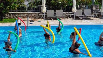 A swimming pool with people exercising with colorful noodles.