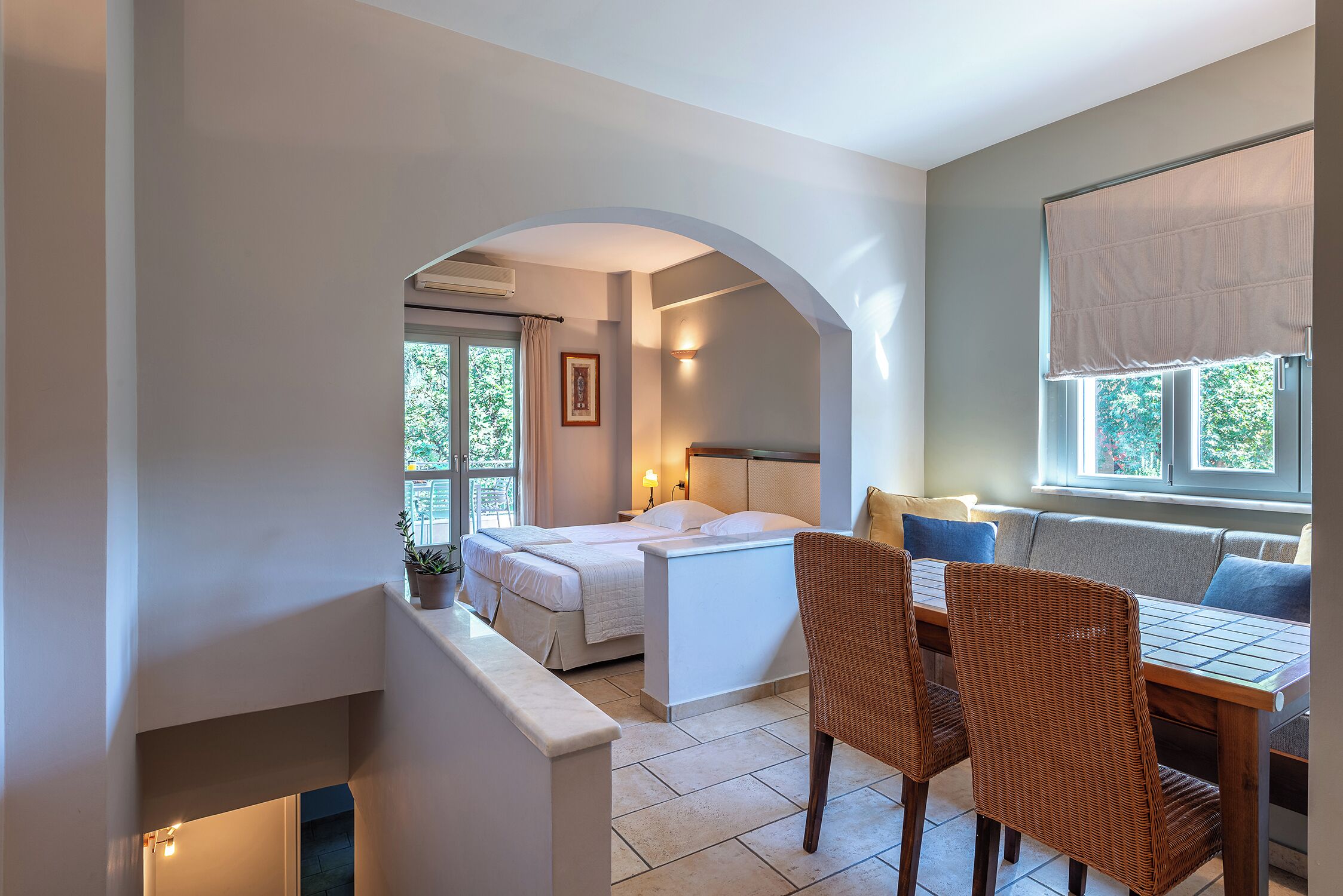Une chambre à coucher avec un lit, un coin salon avec une table et des chaises, et une fenêtre avec un rideau.