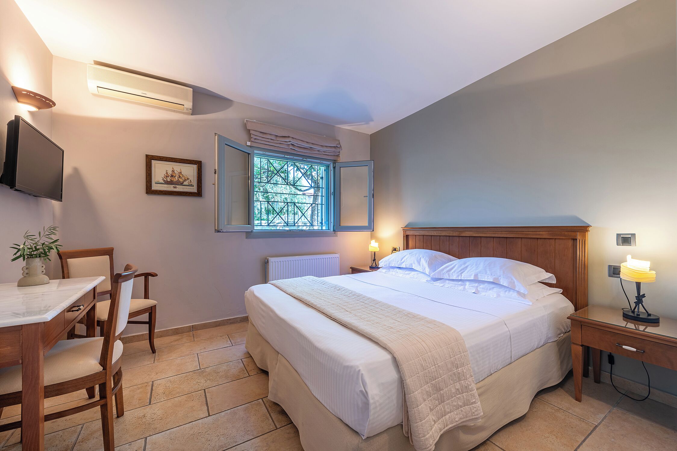 Un dormitorio con cama, mesita de noche, lámpara, ventana y televisor en la pared.