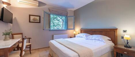 Un dormitorio con cama, mesita de noche, lámpara, ventana y televisor en la pared.