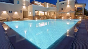 A hotel with a swimming pool, outdoor seating, and a well-lit facade.