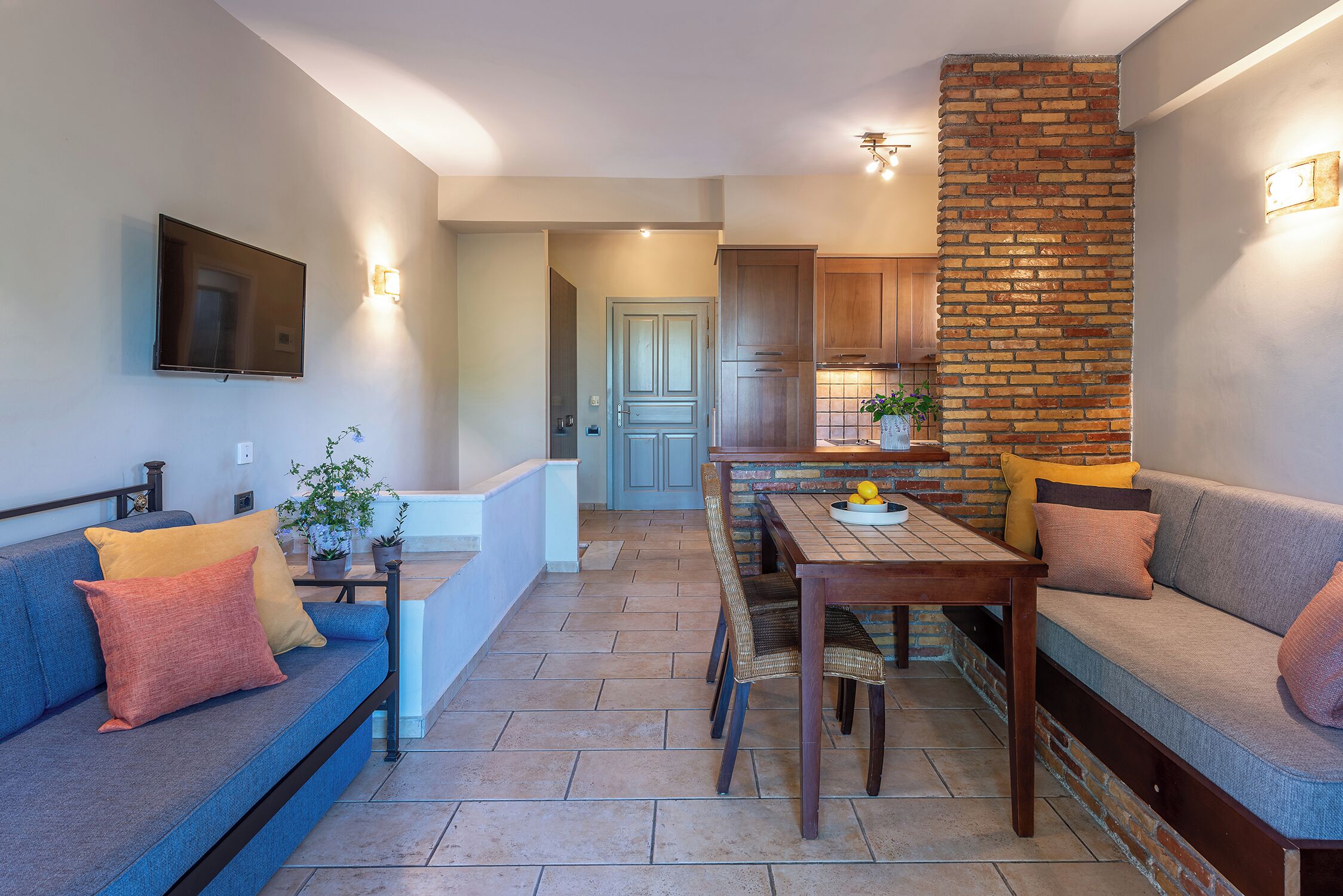 Una sala de estar moderna con un sofá azul, una mesa de comedor de madera y una pared de ladrillo decorativa.