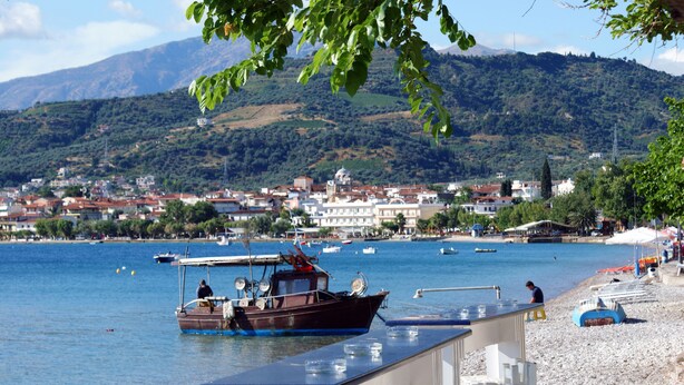 A coastal town with a boat docked on the shore, a pebble beach, and a backdrop of hills.