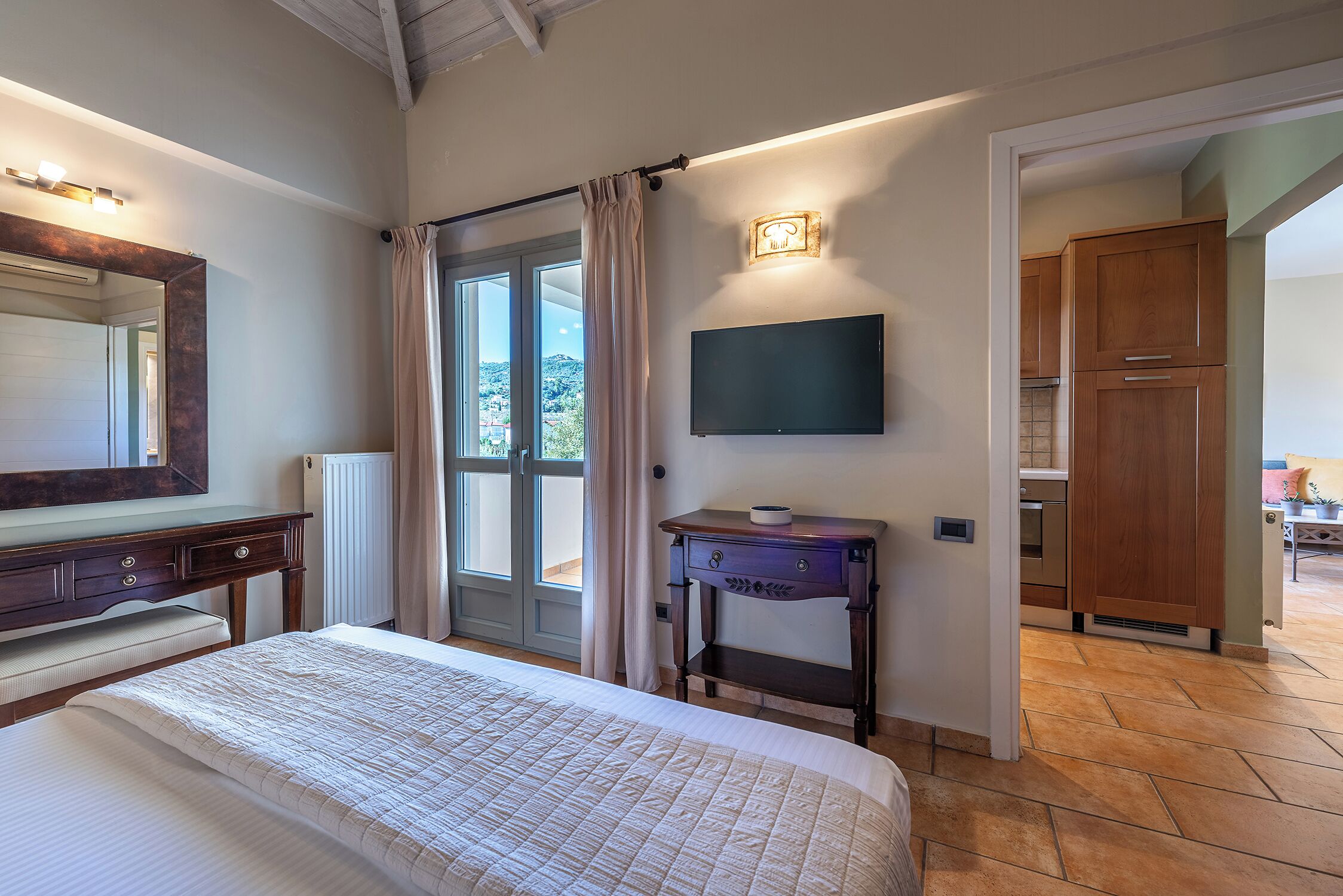 Een slaapkamer met een bed, een nachtkastje, een aan de muur bevestigde televisie en uitzicht buiten door een raam.