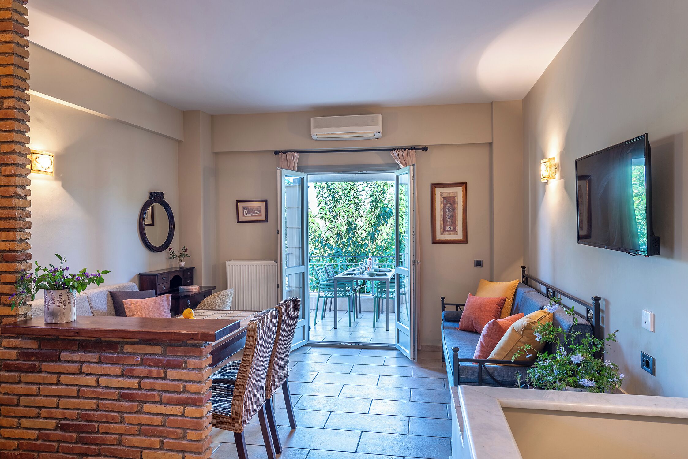 A modern living room with a brick accent wall, a dining area, and a balcony with a view of greenery.