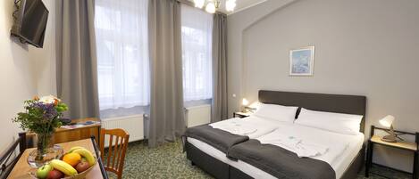 Una habitación de hotel con cama, escritorio con lámpara, una silla, un florero con flores y un frutero.