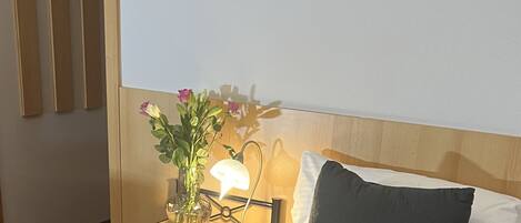 Una habitación de hotel con una cama bien hecha, una mesita de noche con una lámpara, un jarrón con flores y un cuadro en la pared.