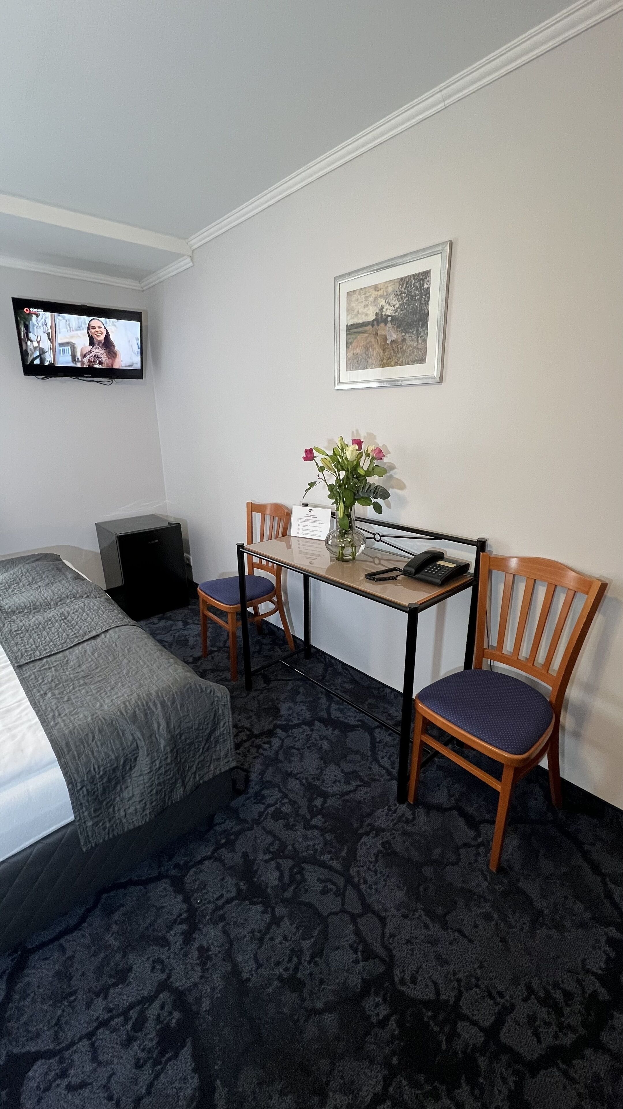 Een hotelkamer met een bed, een bureau met stoel, een televisie en een ingelijst schilderij aan de muur.