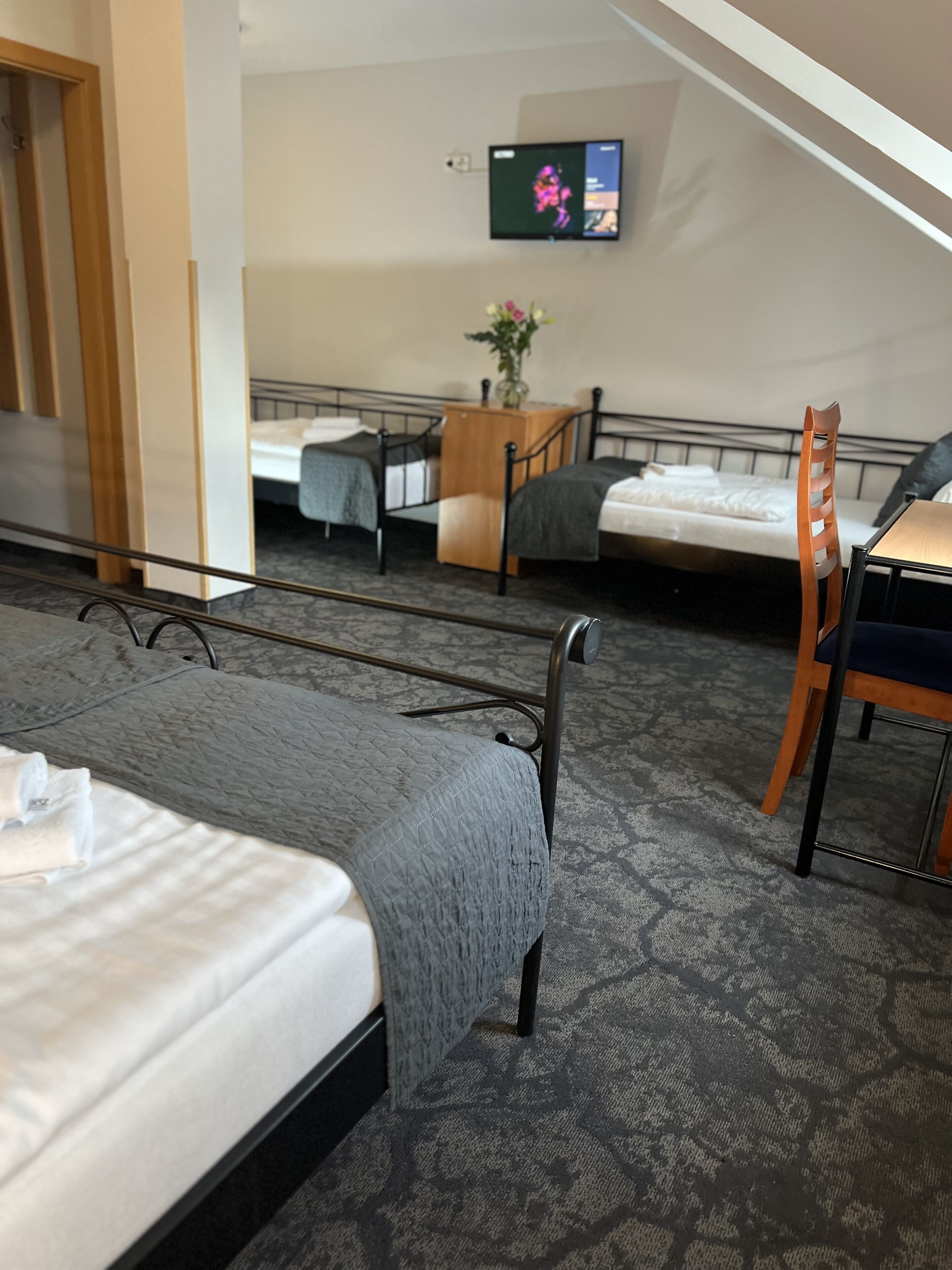A hotel room with two beds, a desk, a chair, a TV, and a small table with a vase of flowers.