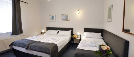 A hotel room with two beds, a radiator, a window with curtains, a chandelier, wall-mounted lights, and a mirror.