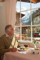Un hombre cenando en una mesa con vistas a montañas nevadas a través de una ventana.