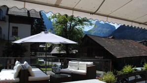 Uma área externa com assentos, um sofá branco, uma mesa e um guarda-sol grande.