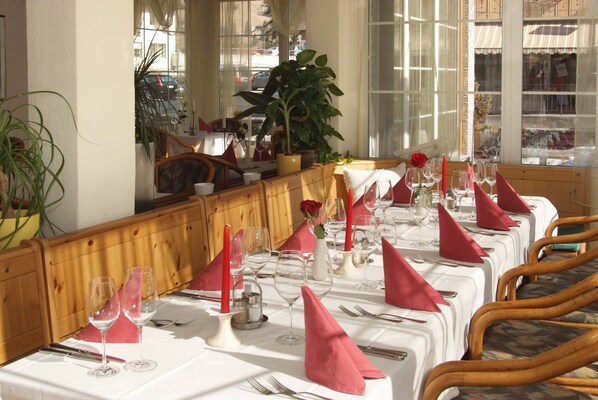 Un espace repas avec des tables dressées pour le service, agrémenté de nappes blanches, de serviettes rouges et de verres à vin.
