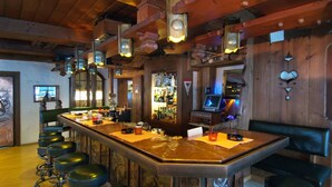 Uma área de bar com um balcão comprido, banquetas e uma adega abastecida com garrafas.