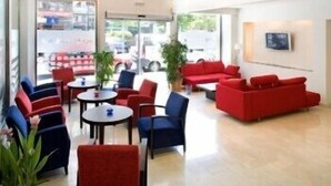 Um saguão de hotel com assentos vermelhos e azuis, grandes janelas e vista para a rua.