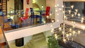 Um interior moderno com uma mesa e cadeiras de vidro, uma escada e um candeeiro decorativo.