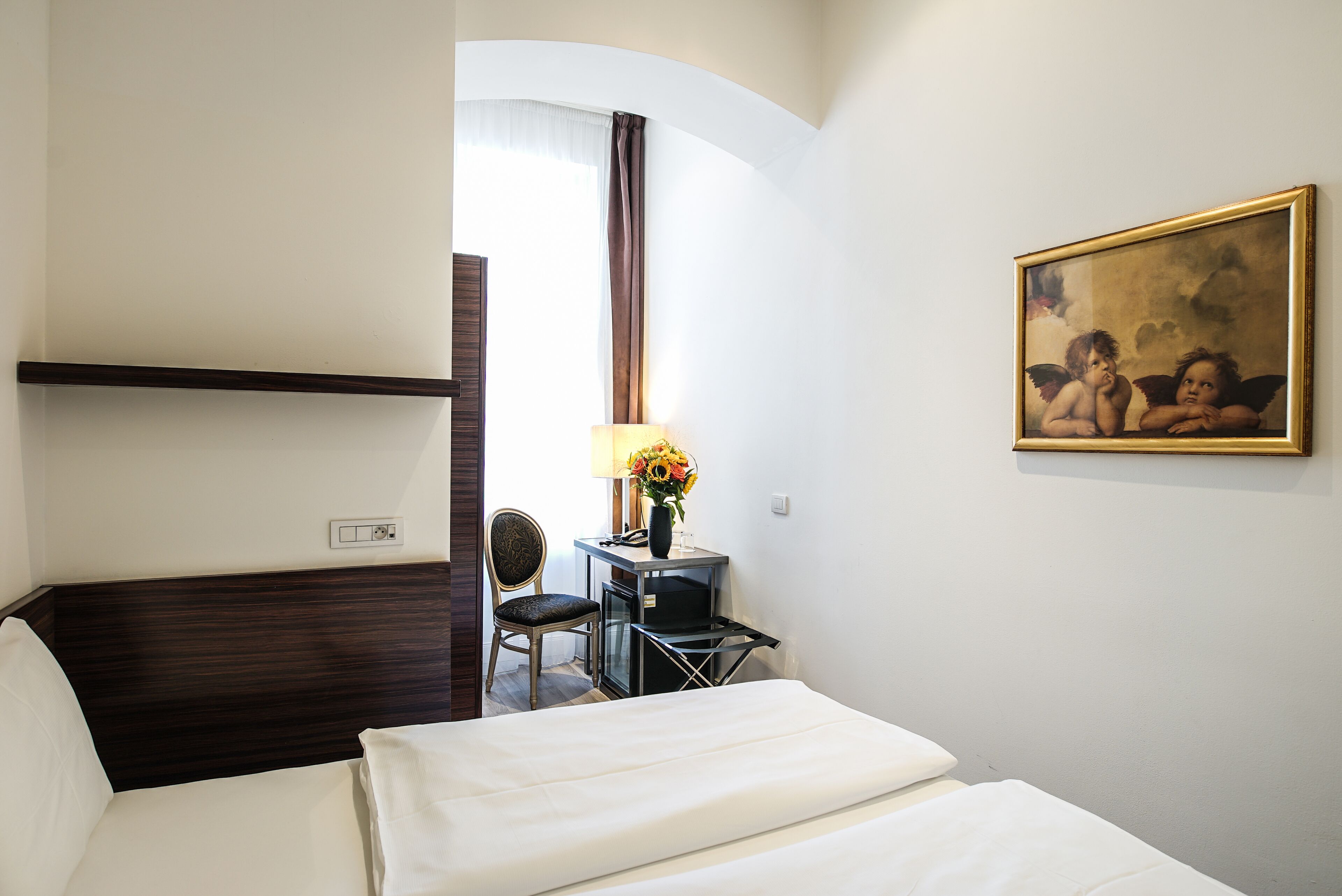 Een hotelkamer met een bed, een bureau met lamp, een stoel en een schilderij aan de muur.
