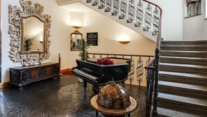 Un vestíbulo imponente con un piano de cola, un espejo decorativo y una escalera con barandillas ornamentadas.