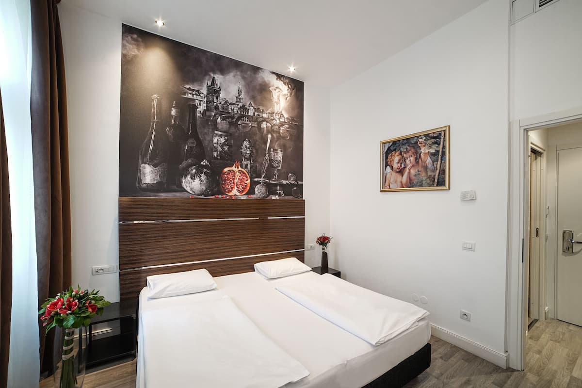 A hotel room with a large bed, a wooden headboard, a wall mural, a framed painting, and a vase with flowers.
