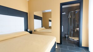 A modern hotel room with a bed, a large mirror, and a glass-enclosed shower area.