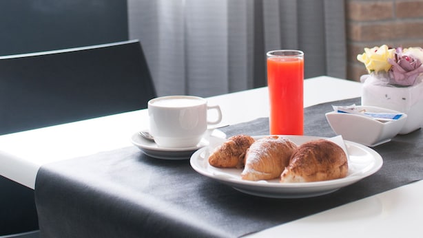 A breakfast table with croissants, a cup of coffee, and a glass of orange juice.