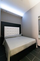 A neatly made bed with a white headboard and a grey bedspread in a hotel room.