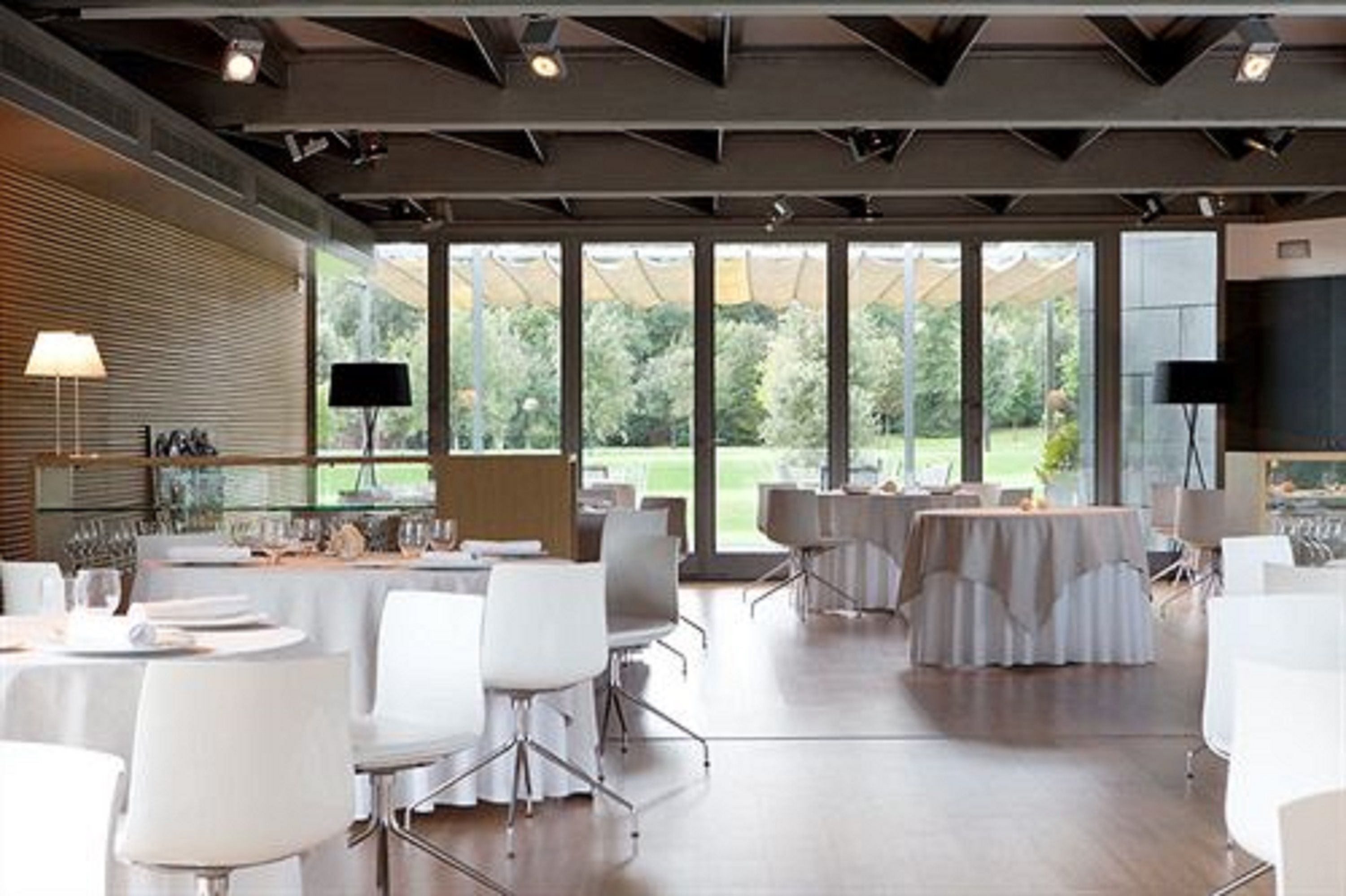 A spacious conference room with tables set for dining, large windows offering a view of greenery, and modern lighting fixtures.