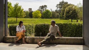 Two people sitting on a concrete ledge with a view of a green park and a distant building.