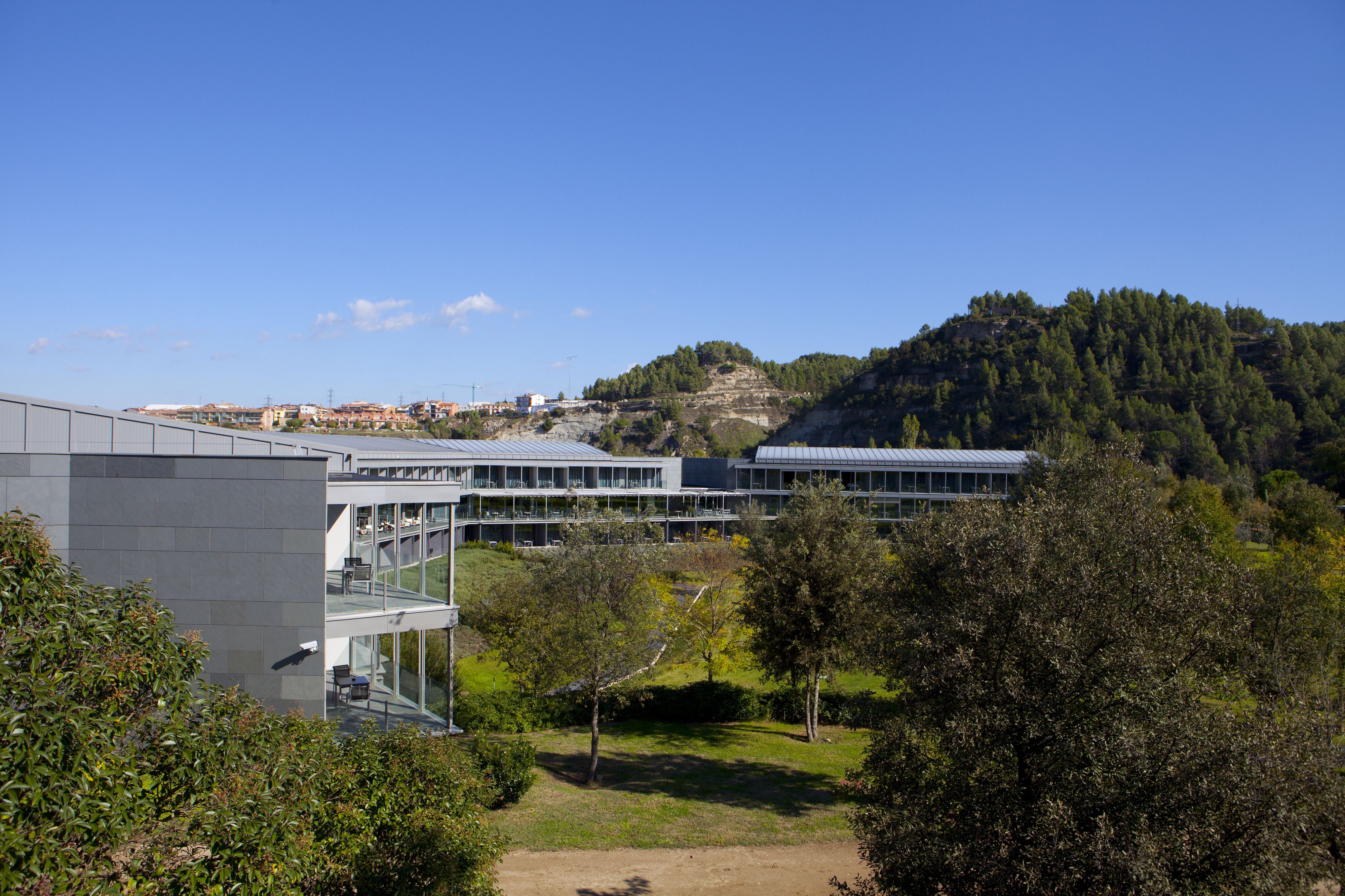Un edificio moderno con fachada de vidrio, rodeado de vegetación y un paisaje montañoso.