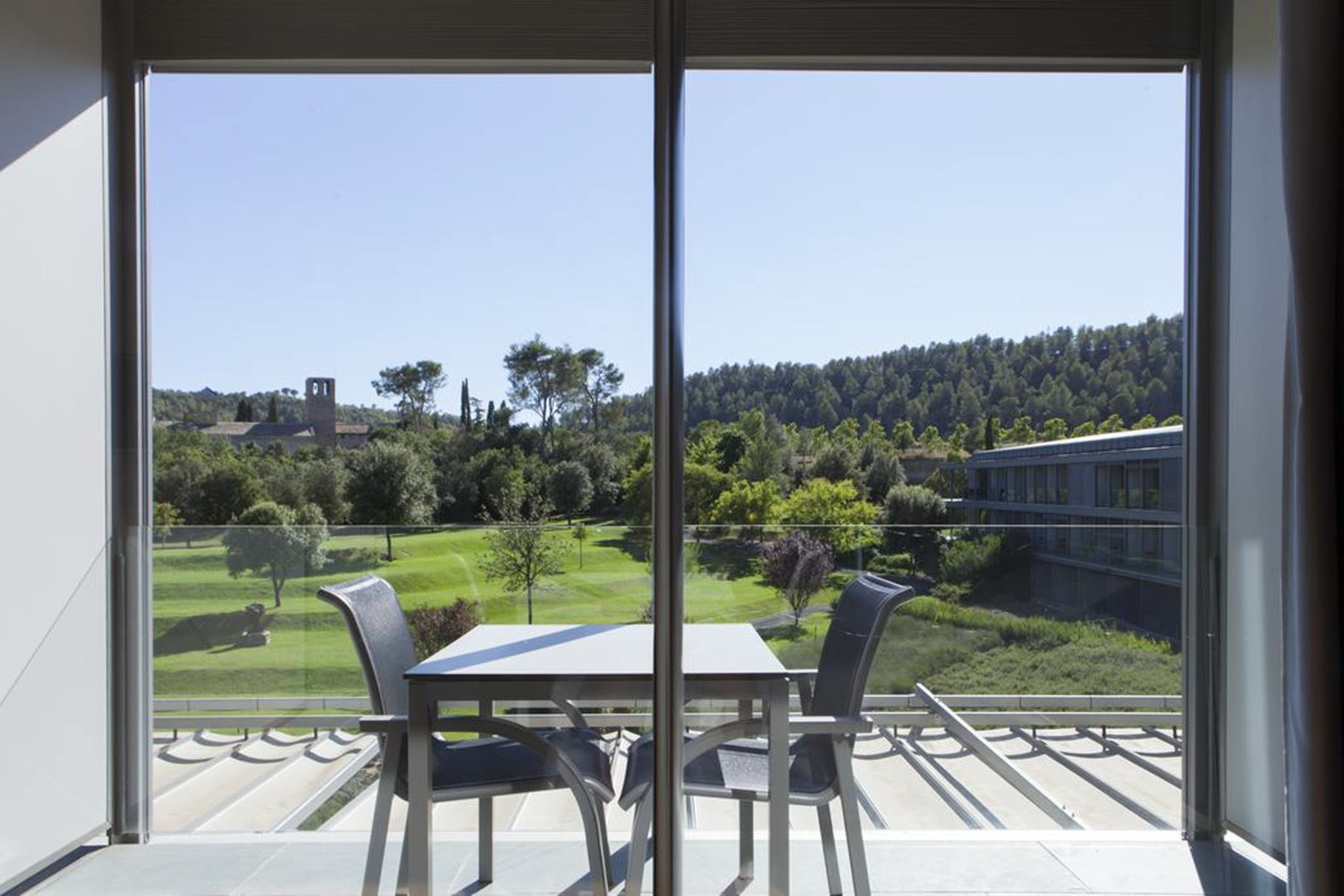 Un balcon avec une table et des chaises, offrant une vue sur un paysage verdoyant et un bâtiment doté d’une tour.