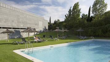 Una piscina al aire libre, sombrillas, sillones reclinables de piscina