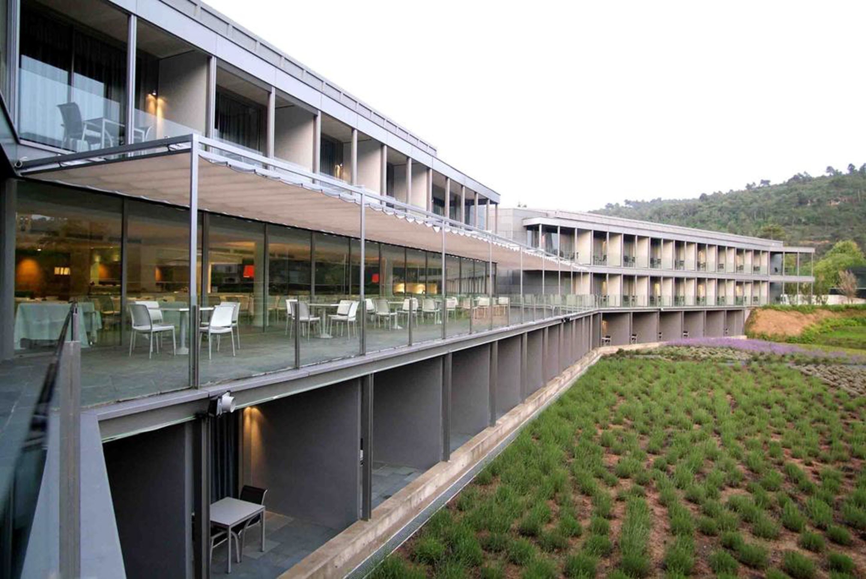 Um edifício moderno com fachada de vidro, área de estar ao ar livre e jardim ajardinado.