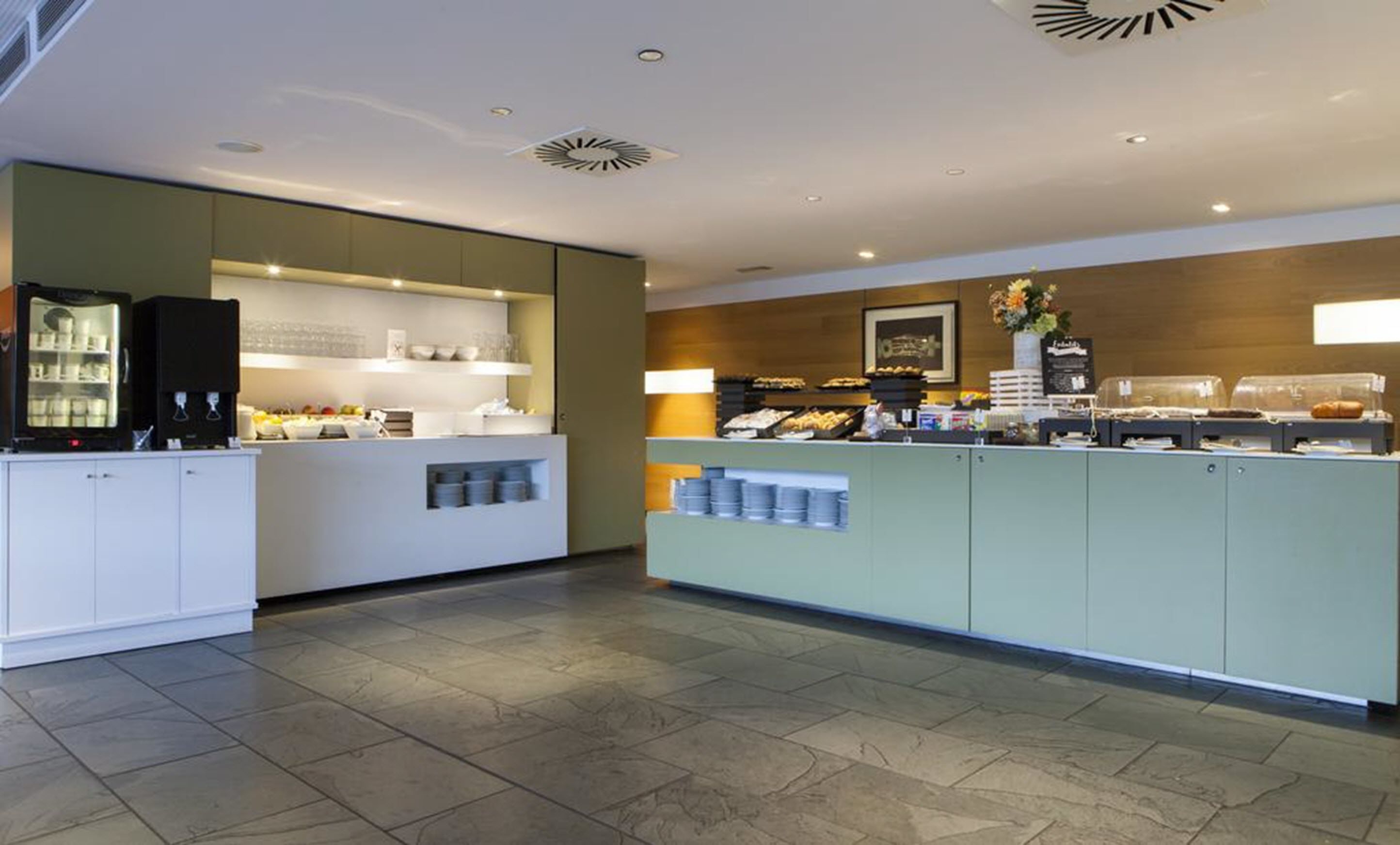 Uma área de refeições moderna com máquina de café, vitrine refrigerada e diversos alimentos.