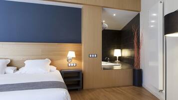 A modern hotel room with a large bed, bedside table, lamp, and a view of the bathroom.