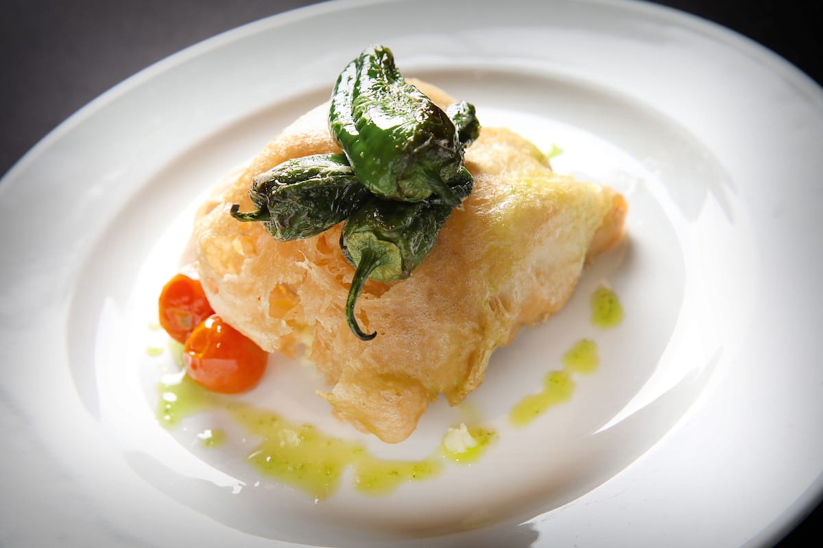 Un plato con una masa crujiente, una guarnición verde y un tomate pequeño.