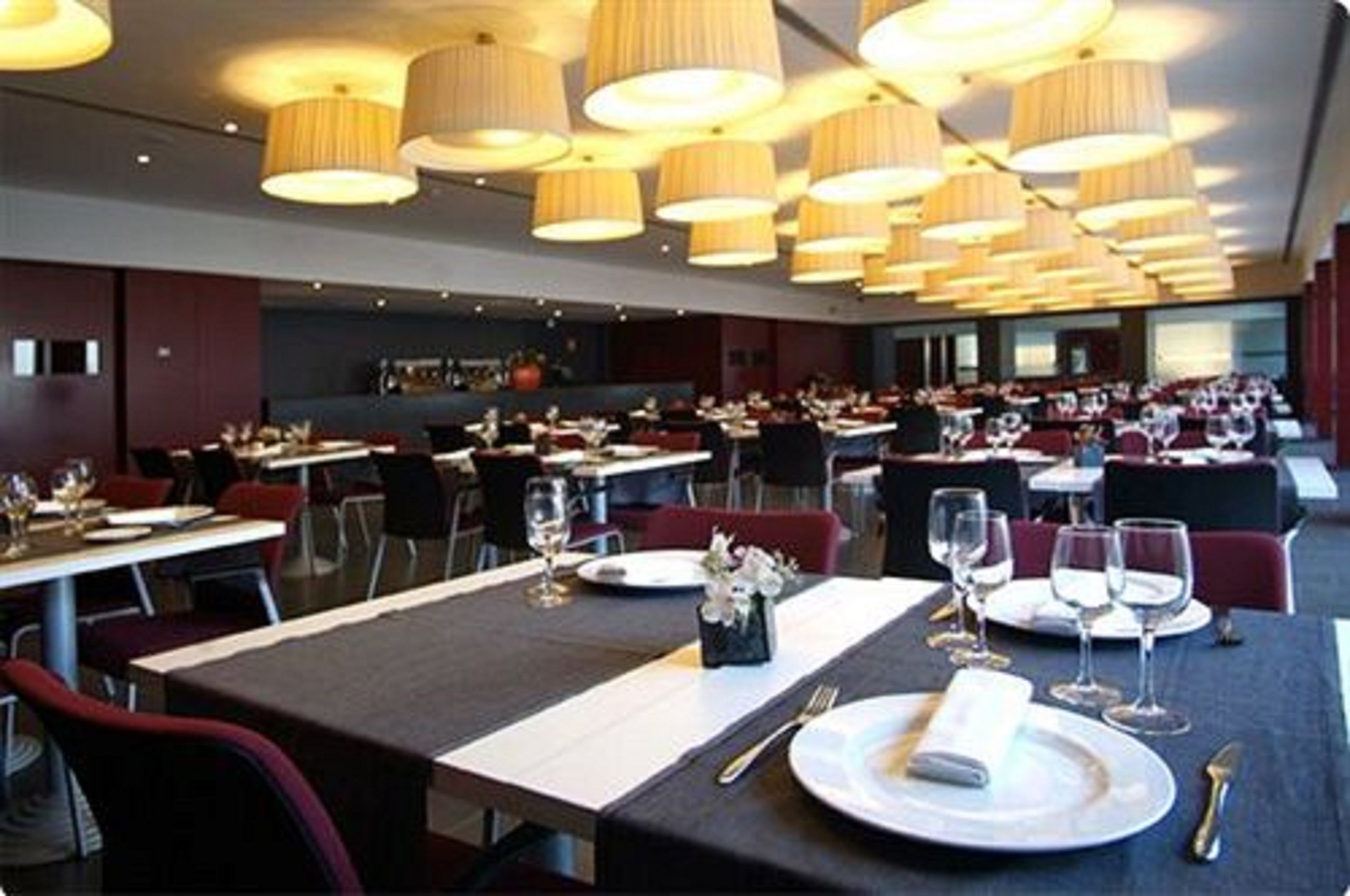 A spacious dining area with multiple tables and chairs, featuring a modern chandelier and a neutral color scheme.