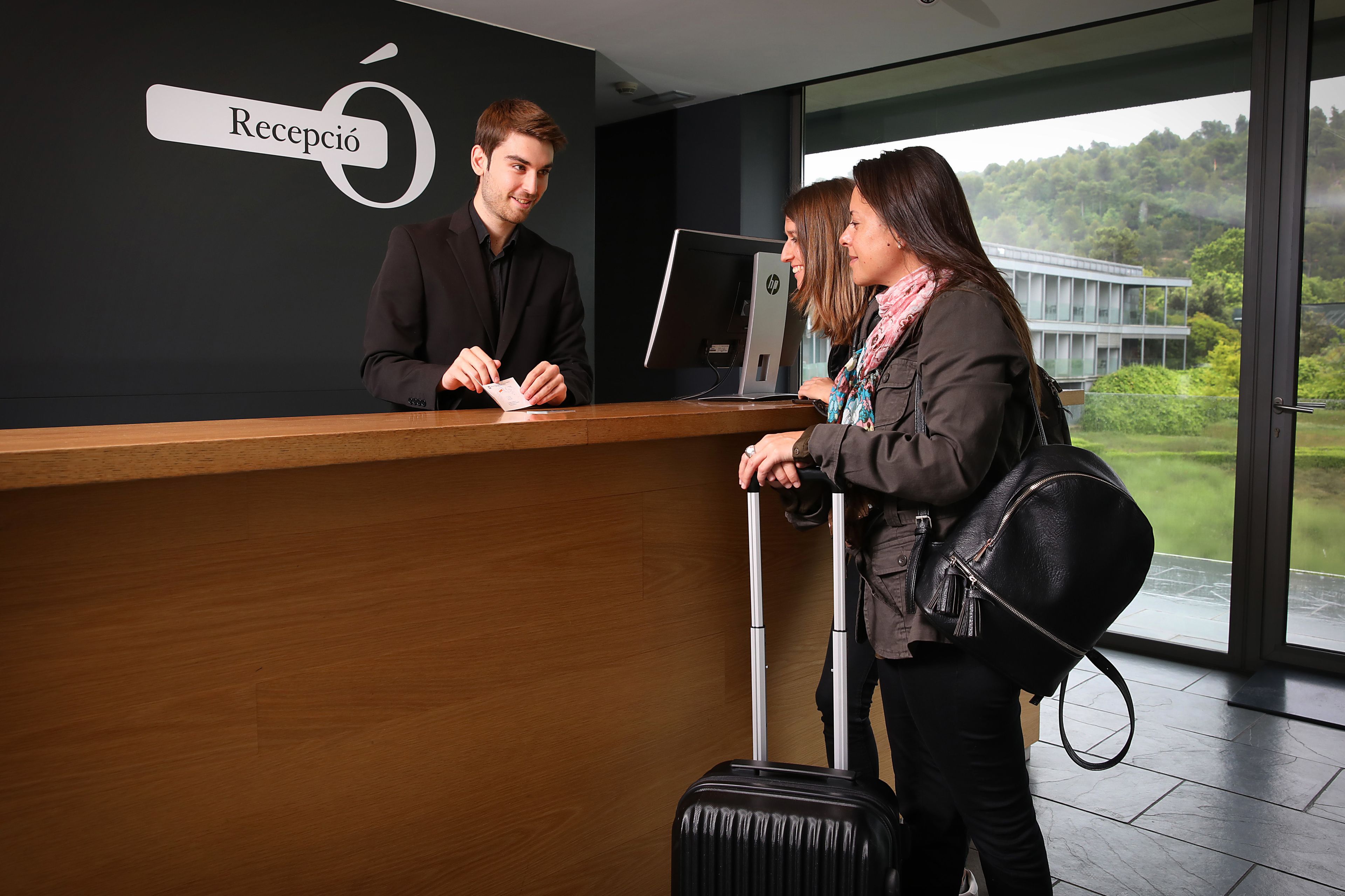 A reception desk with a sign reading "Recepció" in a modern building with large windows.