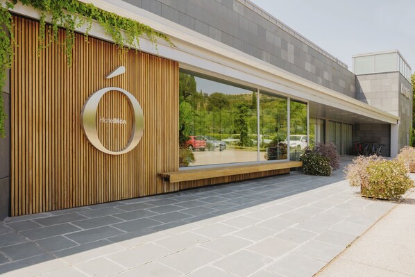 A modern building with a wooden facade, a circular logo, and large windows. - Hotel Món Sant Benet (Sant Fruitos de Bages)