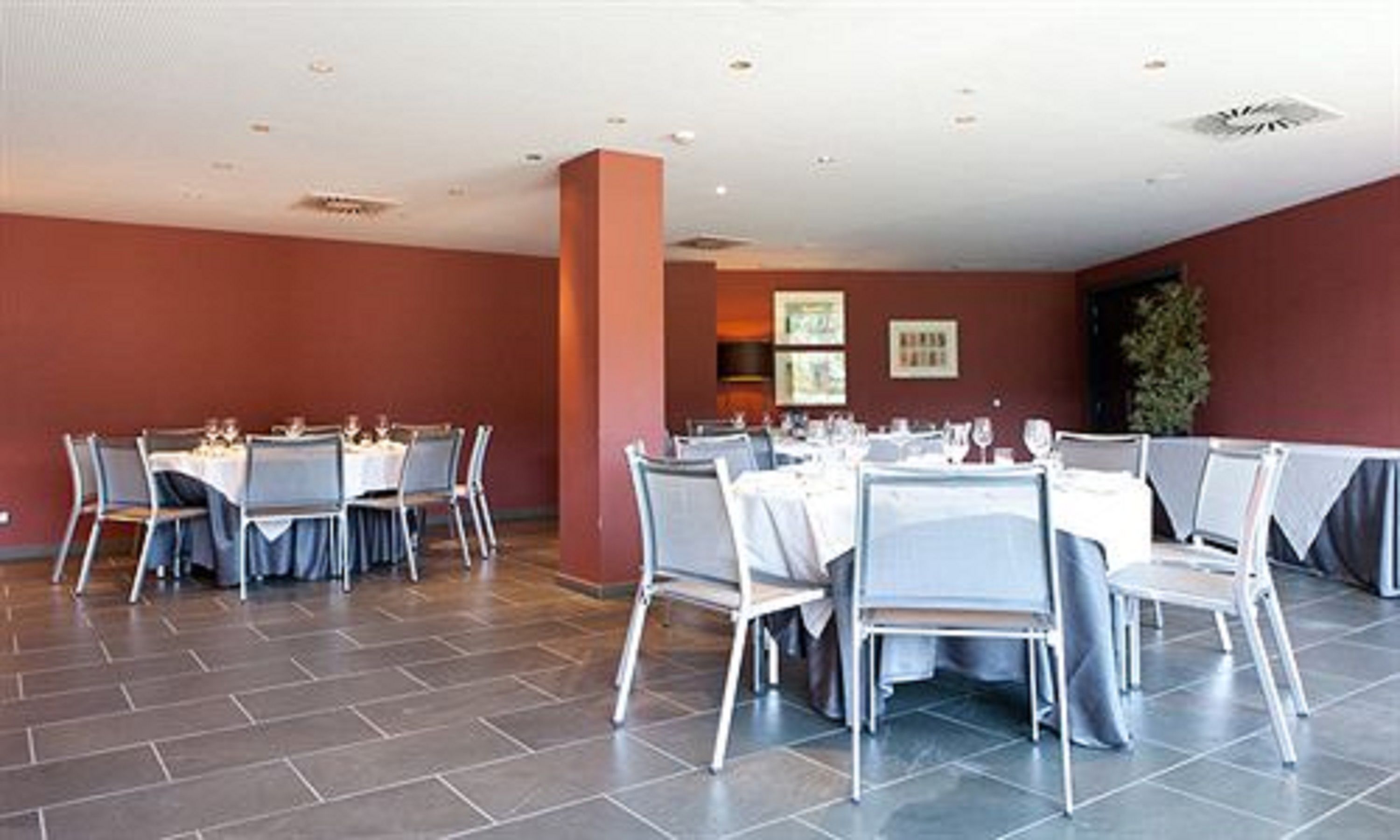 A spacious dining area with multiple tables and chairs, a tiled floor, and a red wall.