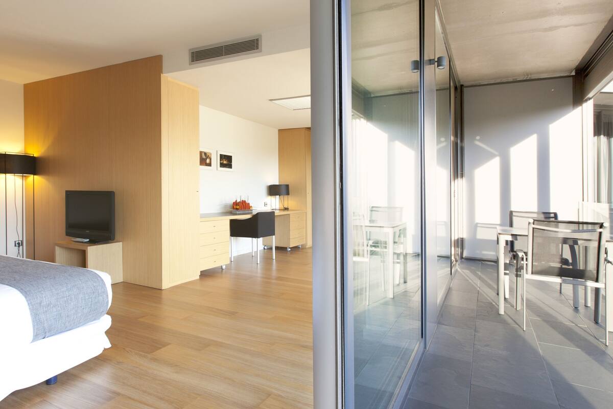 Una habitación de hotel moderna con una cama grande, un escritorio, una silla y un balcón con puertas de vidrio.