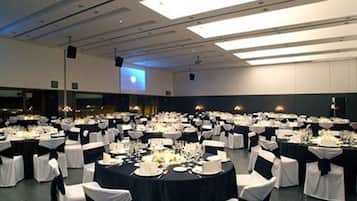 Un amplio salón de banquetes con mesas redondas dispuestas para comer, sillas blancas y manteles negros.